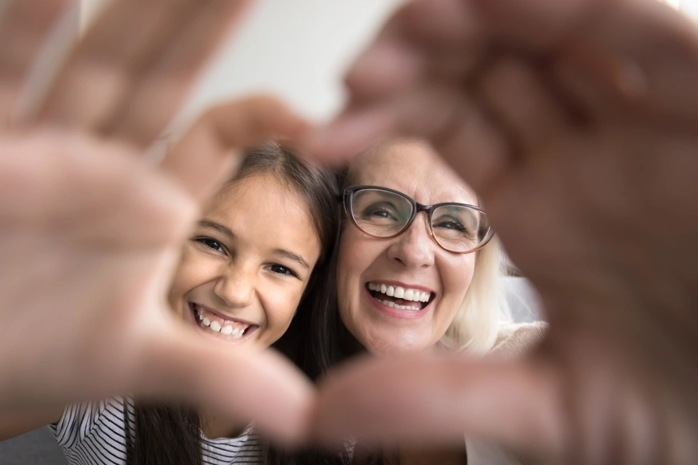 A smiling child and older adult framed by hands forming a heart.